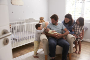 Family With Children And Newborn Son In Nursery