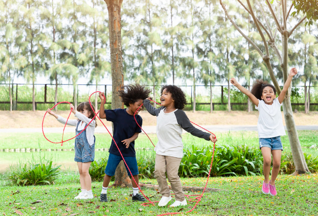 Group of diverse kids playing cheerful in the park. Children having fun and jumping with rope in the garden.