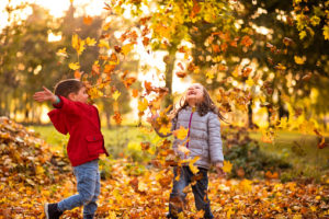 Siblings playing with maple leaves in autumn park at sunset