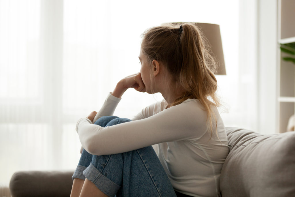 Side view young woman looking away at window sitting on couch