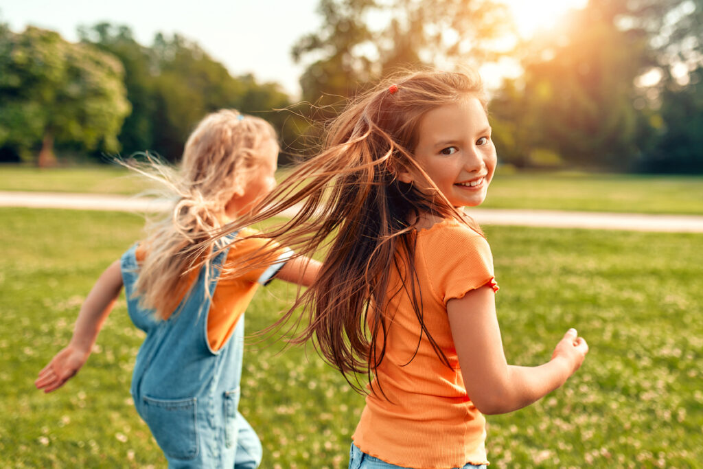 Two cute little sisters children running and playing in the meadow in the park on a warm sunny day, having fun and enjoying nature on a day off.