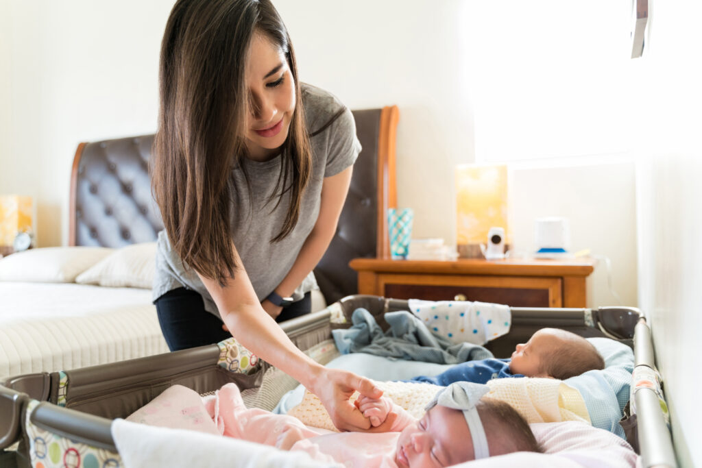 Mother looking at sleeping babies in bedroom at home