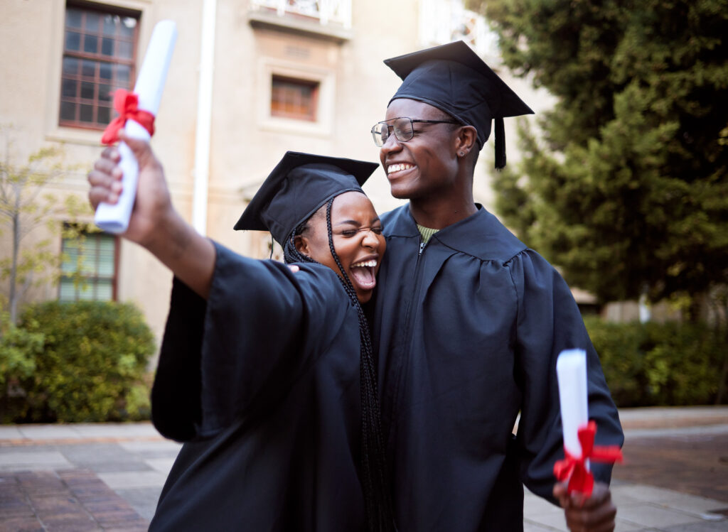 young girl and boy hugging in cap and gown while celebrating with diplomas in hand